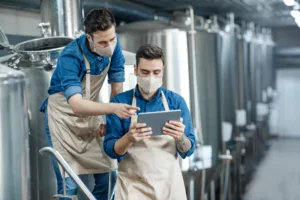 Brewery workers enter data at tablet and operate equipment