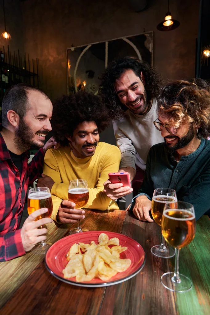Group of friends in a bar having fun, drinking beer, using one phone watching social media.